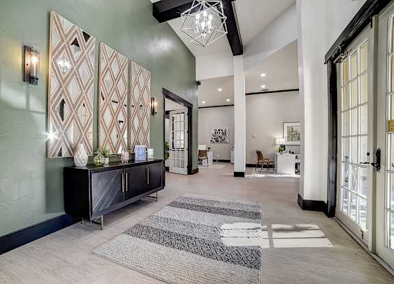 Spacious clubhouse lobby with statement chandelier, patterned wall panels, and seating areas beyond.