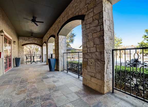 Covered stone-arch patio with tiled flooring, outdoor tables, and wrought-iron railing.