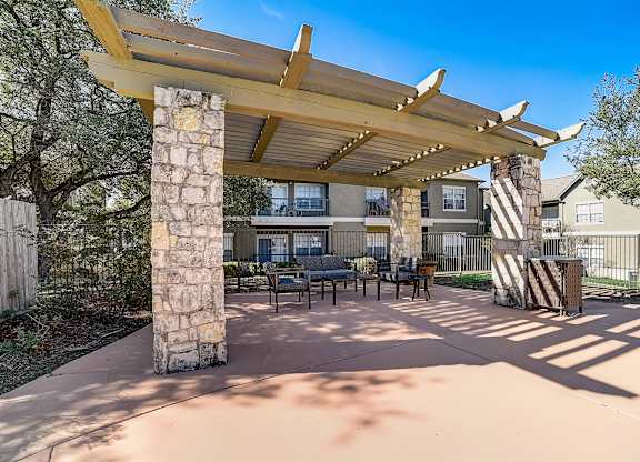 Shaded pergola seating area with stone columns and benches on the pool deck.
