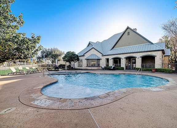 Sparkling pool in front of clubhouse with stone façade and covered patios.