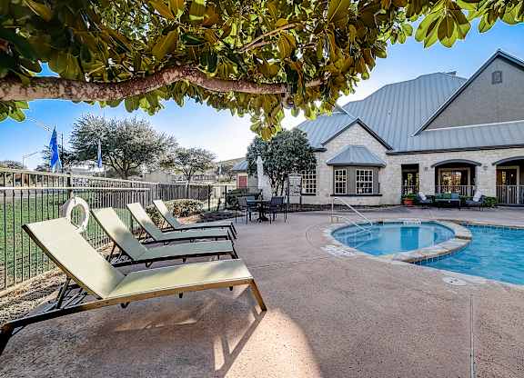 Pool deck with lounge chairs and attached spa beside the stone clubhouse building.