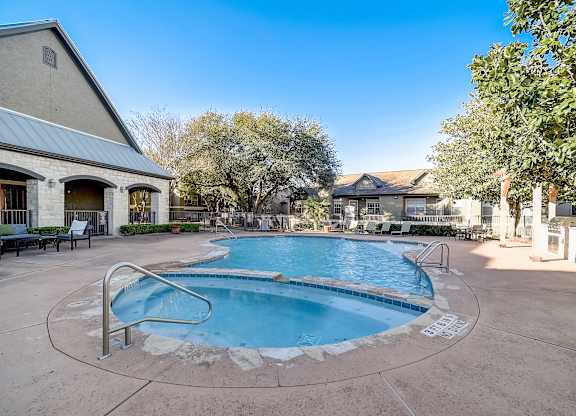 Swimming pool and circular spa with shaded seating and outdoor grilling area nearby.