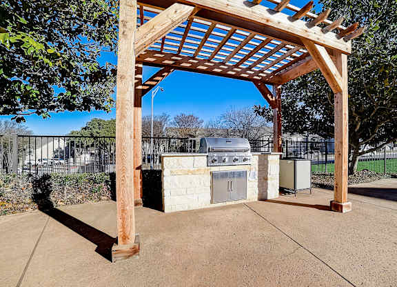 Outdoor grilling station under pergola with built-in gas grill and stone base.