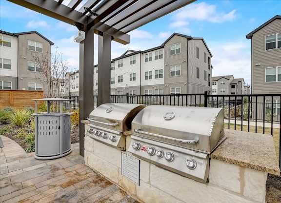 Outdoor grilling area with stainless gas grills, stone counters, and covered pergola for cookouts.
