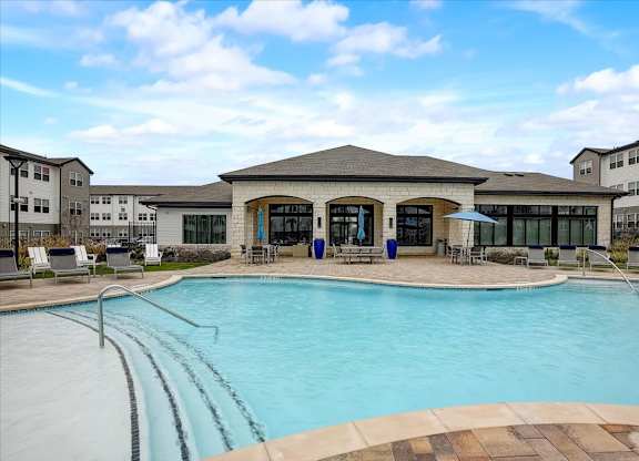 Swimming pool with wide steps, sun deck loungers, and clubhouse backdrop in Hutto, TX.