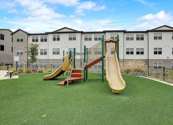Play area featuring multiple slides, climbing platforms, and open turf space inside the courtyard.