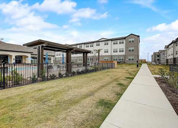 Walking path along the pool courtyard with shaded pergola structure and maintained open lawn.