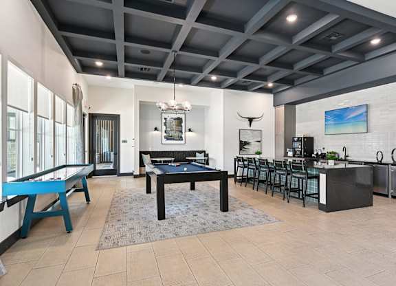 A modern living room with a pool table and a kitchen area.