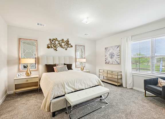 A bedroom with a large bed, a bench, and a window with blinds.