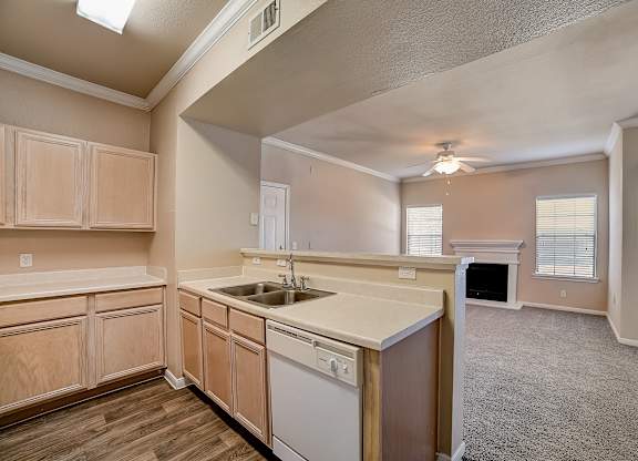 Kitchen sink and dishwasher overlooking carpeted living room with fireplace.