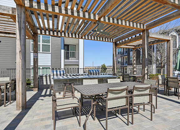 A patio with a table and chairs under a wooden pergola.