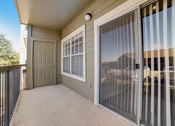 Covered balcony with sliding glass door, vertical blinds, and outdoor storage access.
