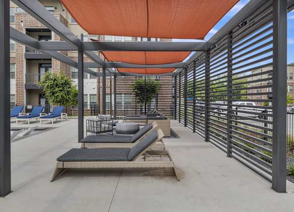 a covered patio with lounge chairs and tables and a metal fence