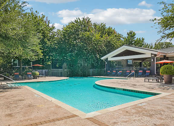 A large outdoor swimming pool surrounded by trees and a building.