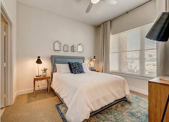 A bedroom with a bed, a nightstand, and a window with blinds.