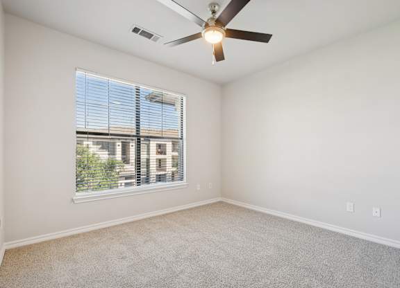 A room with a ceiling fan and a window showing a building outside.