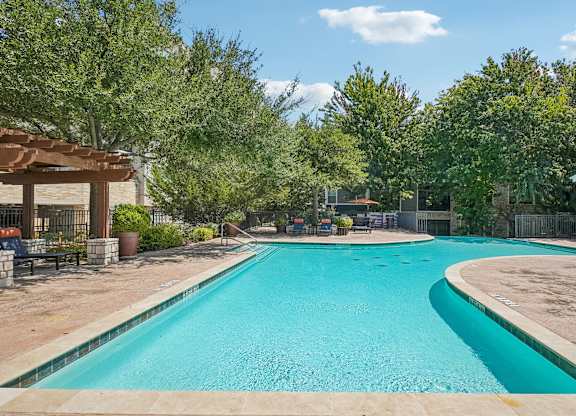 A large outdoor swimming pool surrounded by trees and a fence.