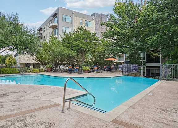 A swimming pool surrounded by trees and a building in the background.
