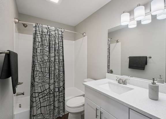 A bathroom with a white sink, toilet, and a shower curtain with a black and white pattern.