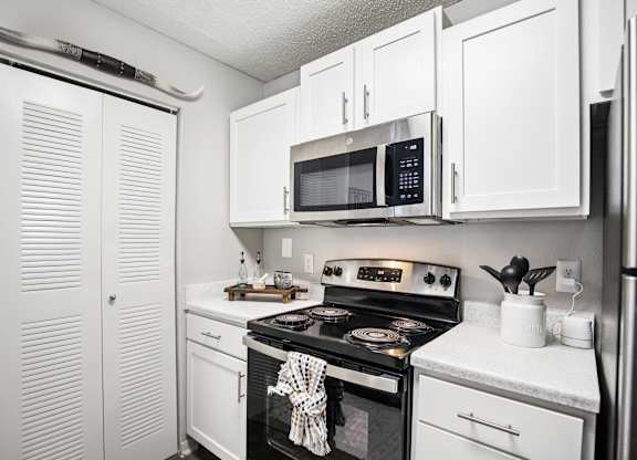 A white kitchen with a black stove top oven and a microwave above it.