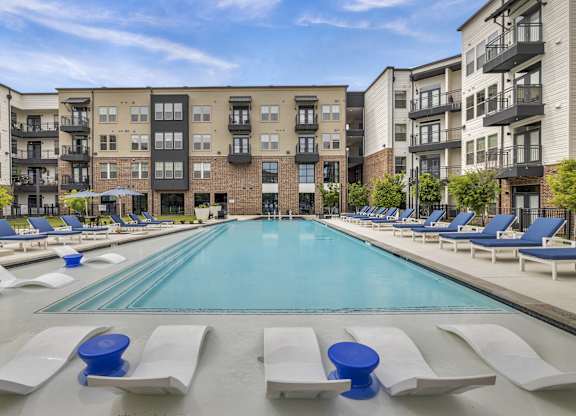 a swimming pool with lounge chairs in front of an apartment building