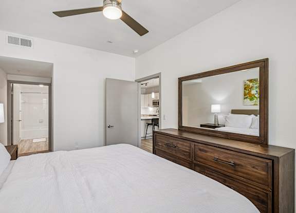 A bedroom with a large bed, a ceiling fan, and a mirror with a wooden frame.