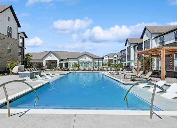 A large swimming pool surrounded by lounge chairs and buildings in the background.