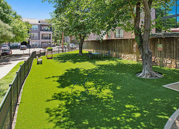 A green lawn with a tree in the middle and a fence around it.