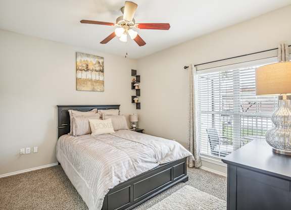 A bedroom with a bed, a ceiling fan, and a painting on the wall.