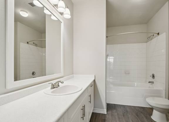 A white bathroom with a sink, mirror, and bathtub.