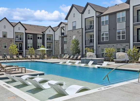 A pool surrounded by lounge chairs and buildings in the background.