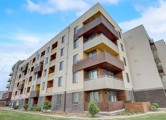 Angled view of multi-story building with wraparound balconies and landscaped courtyard edge.
