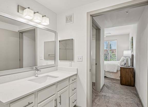 A bathroom with a sink, mirror, and a bedroom in the background.