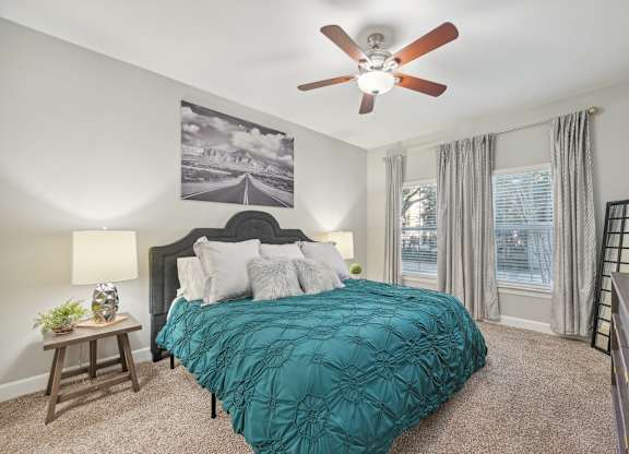 A bedroom with a bed, a ceiling fan, and a painting on the wall.