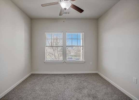 Secondary bedroom with twin windows, ceiling fan, and soft carpeting.