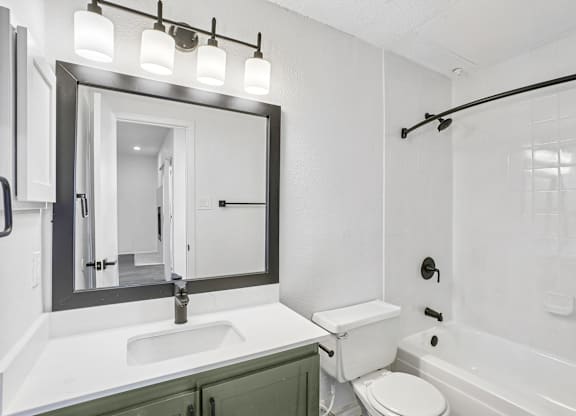 A white bathroom with a green cabinet and a black framed mirror.