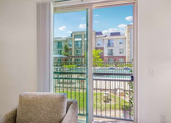 A chair sits in a room with a view of a pool and apartment buildings outside.