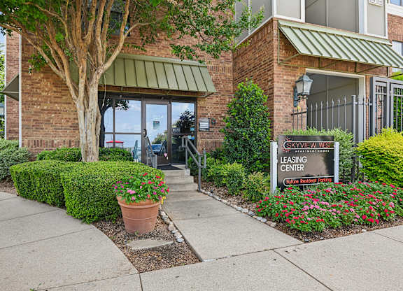 A leasing center sign is in front of a building with a brick facade and a green awning.