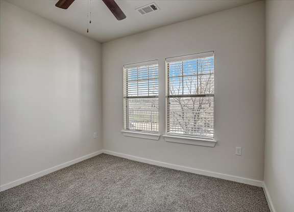 Carpeted bedroom with two windows, white blinds, and ceiling fan.