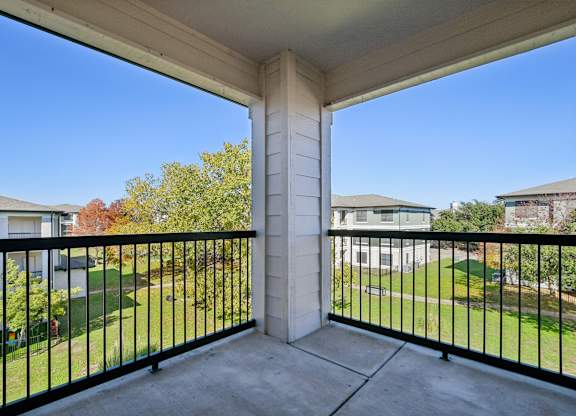 A balcony with a black railing and a view of a green lawn and trees.