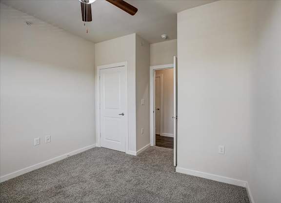Bedroom with plush carpet, ceiling fan, and doorway to hall.