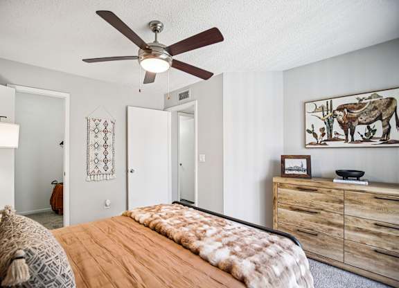 A bedroom with a bed, a ceiling fan, and a dresser.