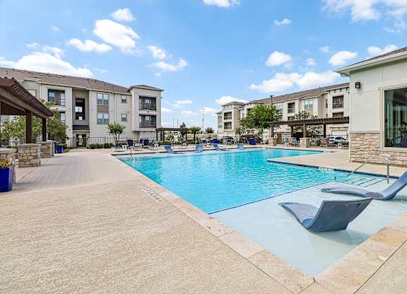 A swimming pool surrounded by lounge chairs and apartment buildings.