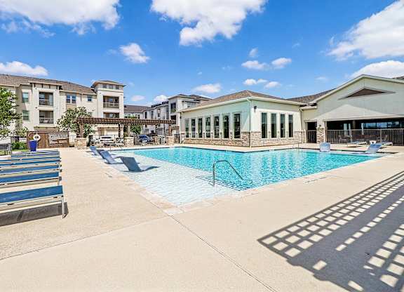 A swimming pool surrounded by a concrete patio and a building in the background.