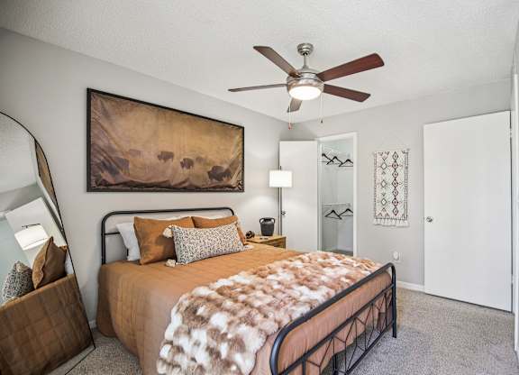 A bedroom with a bed, a ceiling fan, and a painting on the wall.