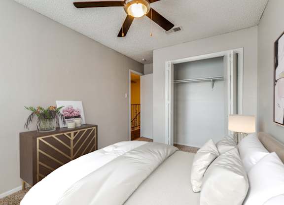 A bedroom with a bed, a ceiling fan, and a dresser with flowers on it.