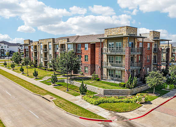 A row of red brick apartment buildings with green trees in front.