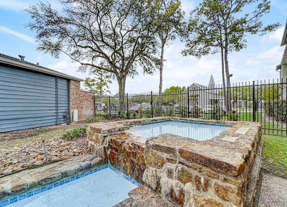 a pool with a stone wall and a fence around it