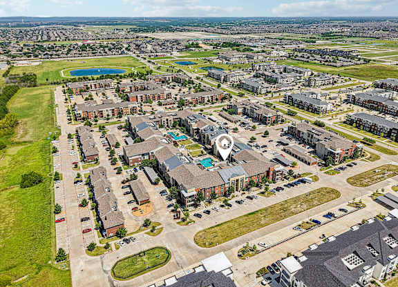 A bird's eye view of a residential area with apartment buildings and a large open space with a pool.
