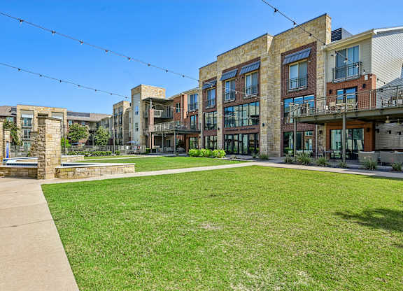 A sunny day in a courtyard surrounded by buildings with a green lawn.
